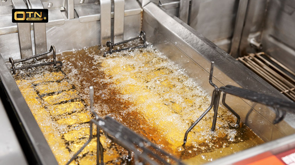  A commercial deep fryer full of oil, actively frying food with baskets partially submerged, in a busy restaurant kitchen setting.