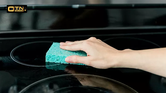  A person's hand cleaning a black stove using a green sponge