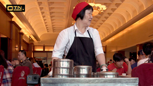 A waitress woman in a red hat standing behind a metal cart carrying cutlery