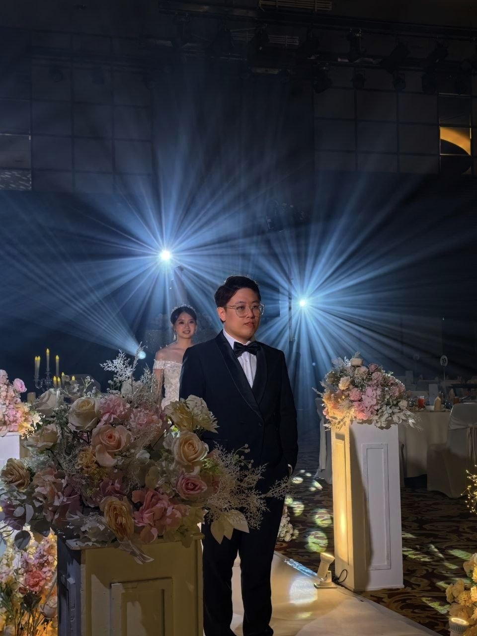 Dramatic backlighting creates a radiant starburst effect behind the groom, casting a luminous glow that highlights the celebratory atmosphere of the wedding aisle.