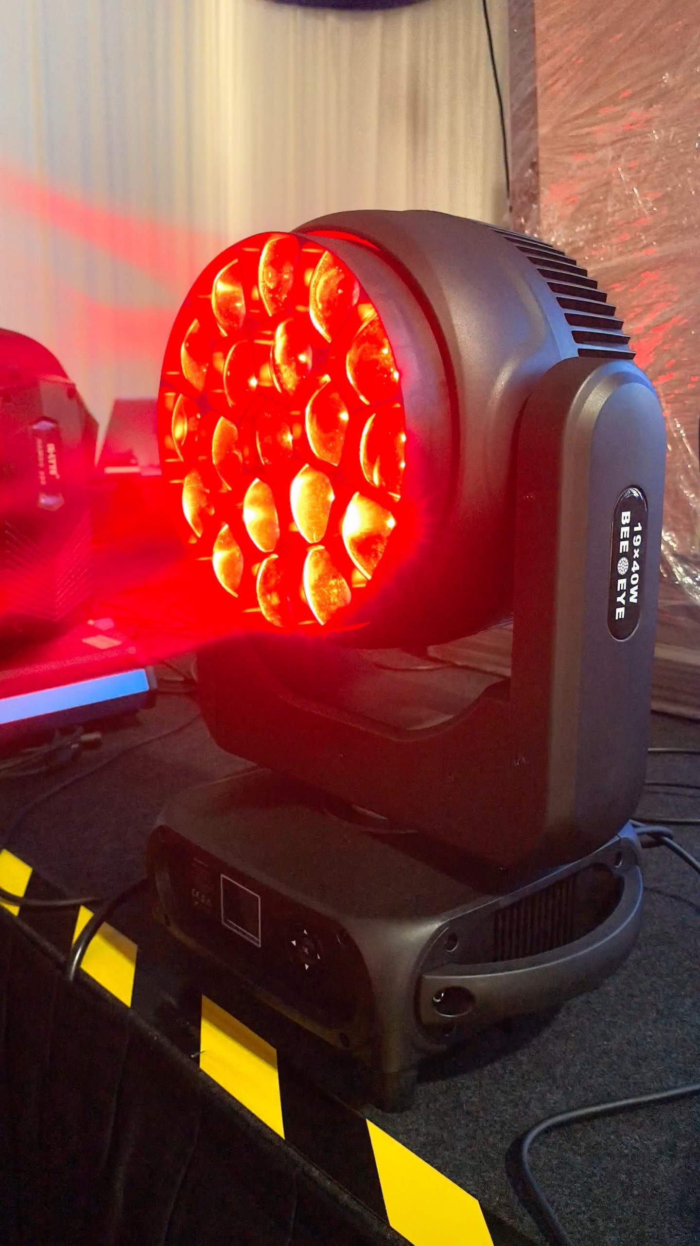 A high-angle shot of a professional Bee Eye 19x40W stage lighting fixture, featuring a circular honeycomb lens array glowing with intense red light.