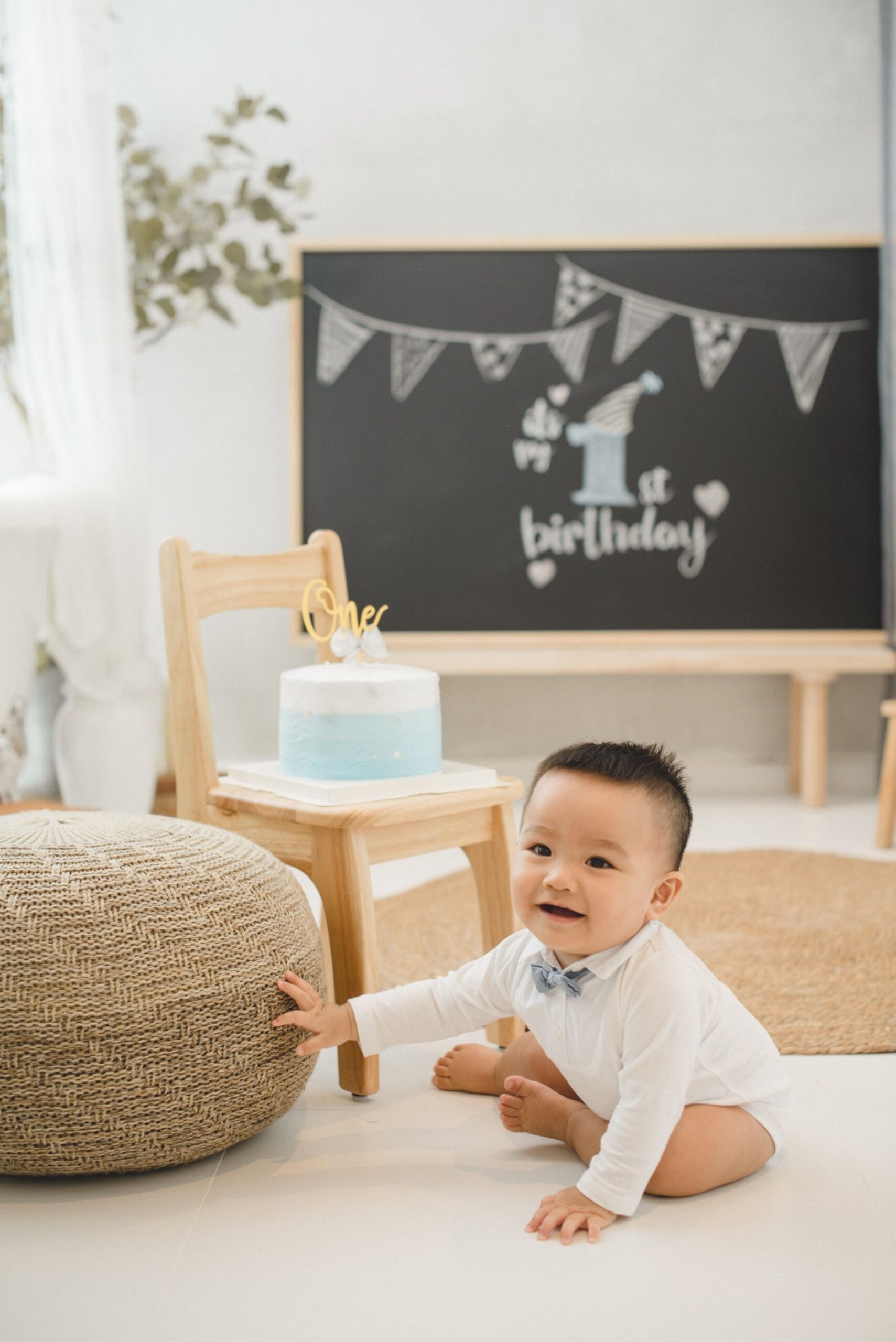Cake smash portrait of baby beside birthday cake in a bright studio birthday setup