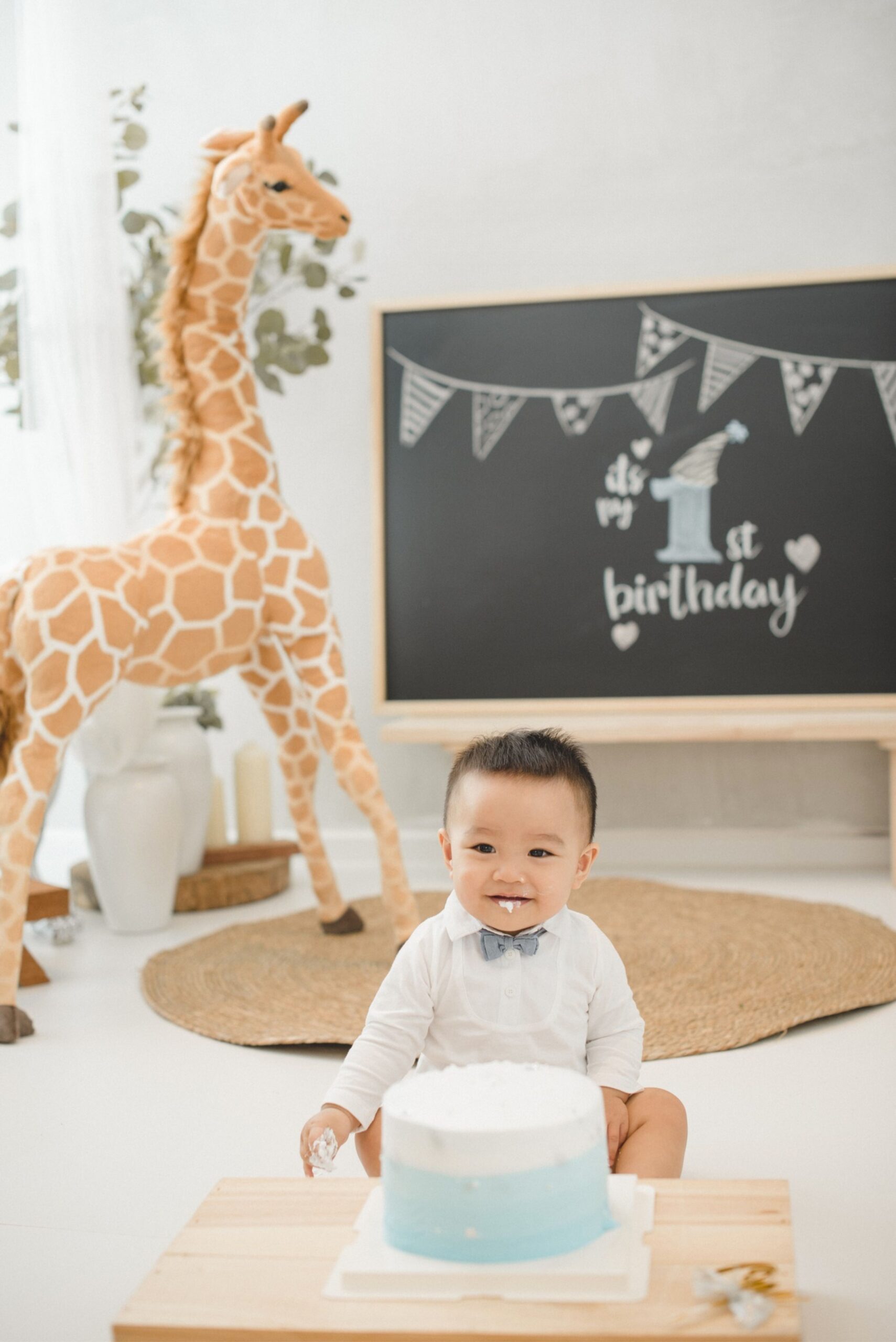 First birthday cake smash portrait with baby smiling in front of birthday backdrop