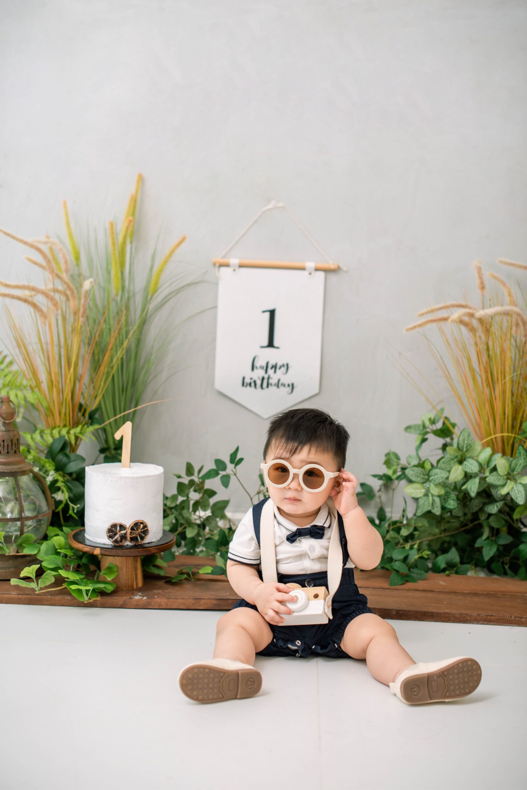 Cake smash photo of baby with sunglasses and birthday cake during milestone session