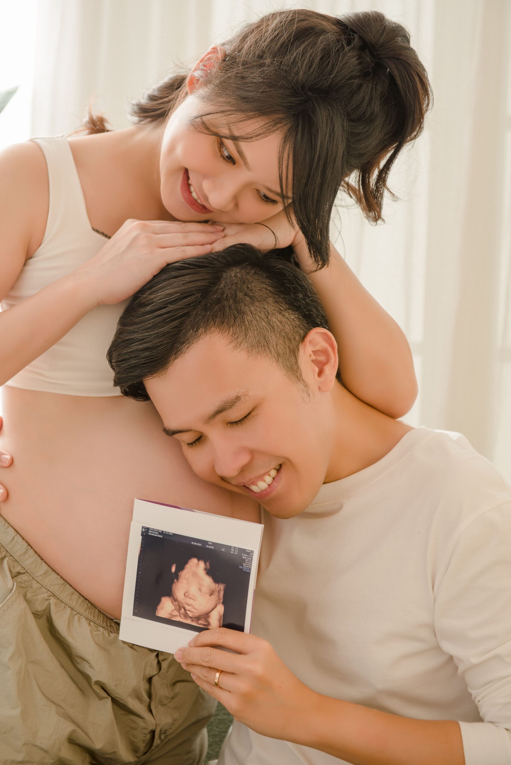 Maternity photography with couple holding baby ultrasound photo in warm natural light